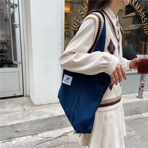 Dark blue canvas tote bag with white patch detail shown in a street style outfit