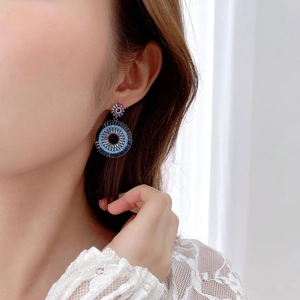 Close-up of circular earrings with blue and purple zircons worn by a model
