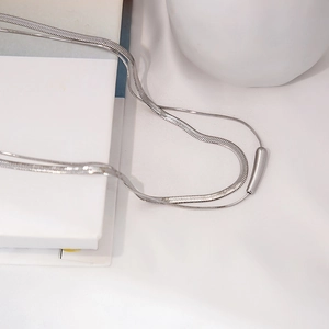 Close-up of minimalist layered silver snake chain and cylinder pendant on white aesthetic decor
