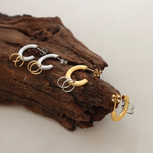 Minimalist gold and silver interlocking hoop earrings on a textured wooden branch display
