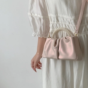 Pink pleated cloud handbag with pearl bead handle and shoulder strap worn by model
