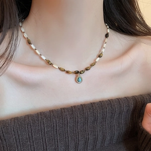 Detail of beaded necklace with cream bars and teardrop turquoise pendant on a model