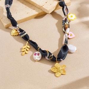 Detail of silk scarf necklace with leopard print and mixed charms on beach sand