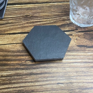 Hexagonal dark grey slate coaster on a rustic wooden table with a glass water cup