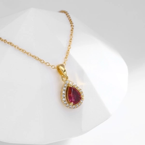 Macro detail of a gold necklace featuring a pear-cut red gemstone with a diamond halo
