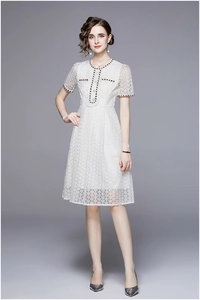 Detail of white lace midi dress featuring black gold trim and pearl buttons on neckline
