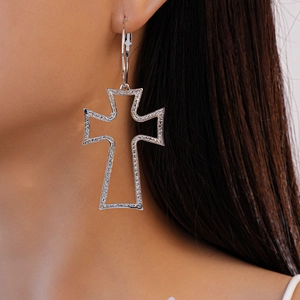 Close-up of a silver-colored hollow cross earring worn by a model with a textured finish