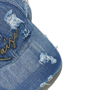 Detail of distressed denim baseball cap featuring gold embroidery and metal ring accents