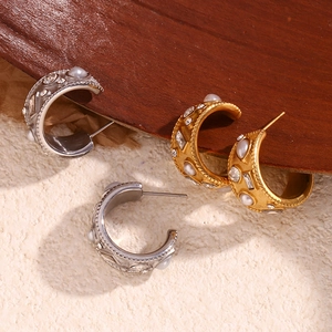 Detailed view of C-shaped earrings with 18K gold plating, pearls, and crystals on wood