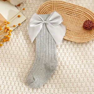 Détail de chaussettes bébé en maille côtelée gris clair avec grand nœud en satin sur plateau