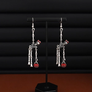 Detail of Halloween skeleton earrings with red bow and pumpkin on a black display stand