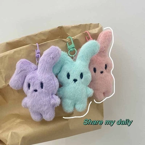 Detailed shot of cute plush bunny keychains in pink, purple, and mint green on a bag
