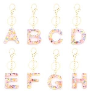 Flat lay of resin letter A to H keychains with colorful sequins and gold lobster clasps