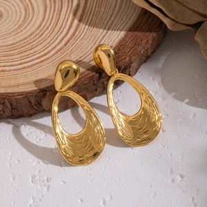 Golden wavy textured teardrop earrings displayed on a rustic wood piece with dry leaves