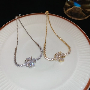 Close-up of gold and silver clover bracelets with zircon stones on a white plate