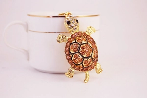 Close-up of golden metal turtle keychain with sparkling orange rhinestones and black eyes