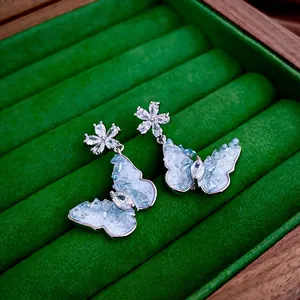 Elegant silver butterfly and flower drop earrings with blue crystals on green velvet