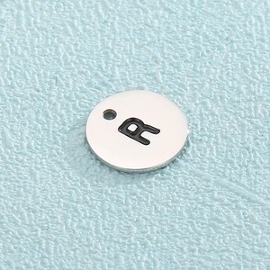 Macro view of silver stainless steel round pendant with letter R engraving detail