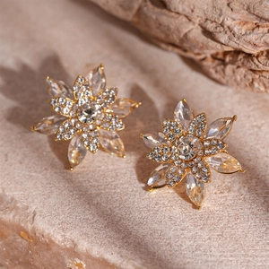 Macro shot of gold floral earrings with crystal petals on a natural stone surface