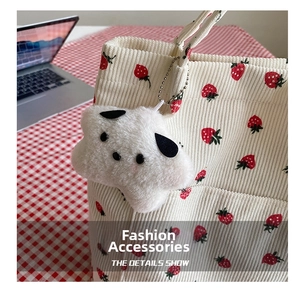 Detail of white plush dog charm on a white corduroy bucket bag with strawberry print