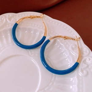 Détail des boucles d'oreilles C bleu et or sur une assiette en céramique texturée