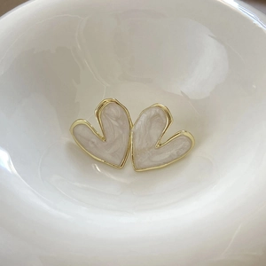 Elegant heart-shaped gold studs with cream marble texture in a ceramic dish