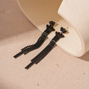 Macro detail of dark-style tassel earrings with black crystals on a stone prop