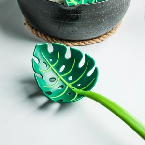 Macro detail of a green monstera leaf slotted spoon for serving food in a ceramic bowl