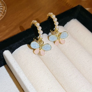 Détail de boucles d'oreilles papillon dorées avec perles et cristaux dans un écrin en velours