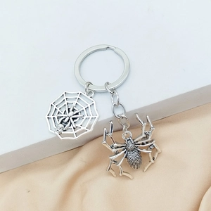 Silver metal Halloween spider and web keychain on neutral fabric background
