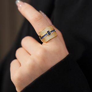 Detail of gold-plated wide band ring featuring blue rectangular stone and white zircon