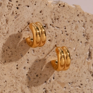 Detailed macro view of double-layered gold C-shaped hoop earrings on a stone base