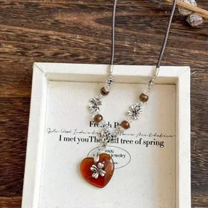 Macro detail of amber resin heart pendant with silver flower on a beaded cord necklace