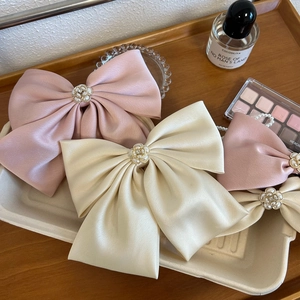 Detailed view of satin bow hair clips with pearl camellia centers in pink and beige