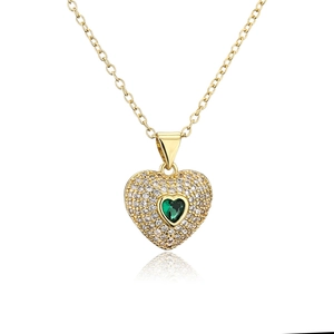 Detail of gold heart necklace featuring pavé white stones and green gemstone center