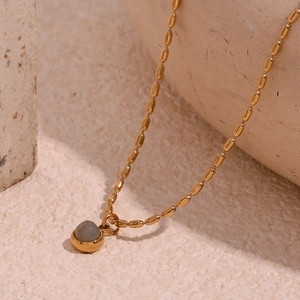 Macro detail of 18K gold-plated beaded chain and gray-blue gemstone pendant on a stone surface