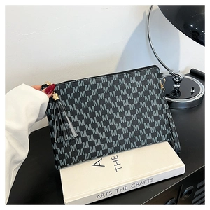 Detail of black monogram envelope bag featuring grey M pattern and tassel zipper pull