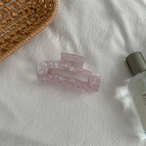 Detail of pink marble acetate hair claw clip on soft white linen background