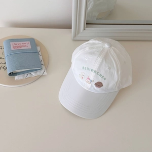 Détail de broderies d'ours et de lapin sur une casquette en coton blanc pour enfant