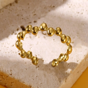 Close-up of golden beaded open ring on beige stone showing metallic luster and texture