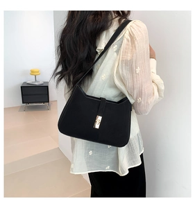 Model wearing black suede shoulder bag with gold clasp and minimalist rectangular design