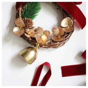 Detail of Christmas wreath with golden bells, pine cones and red velvet ribbons on white