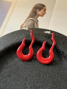 Detail of red flame-shaped stud earrings with glossy finish on a textured black tray