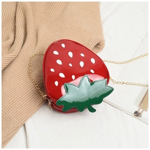 Detailed macro view of a strawberry shaped red patent leather bag with gold chain strap