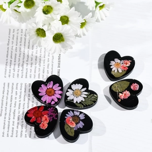 Vista macro de dijes de corazón de resina negra con flores secas reales para joyería artesanal