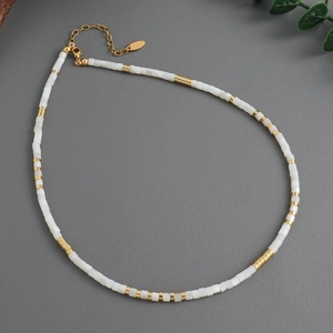 Minimalist white shell beaded necklace with gold plated brass accents on textured background