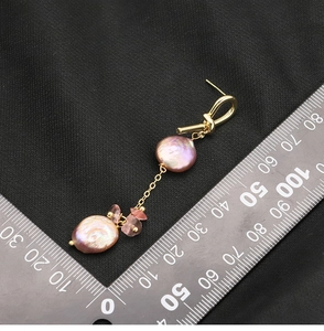 Macro view of long baroque pearl earrings with gold chain and size ruler on black fabric