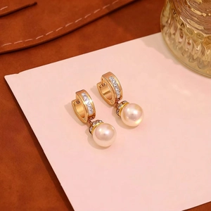 Macro shot of gold-plated pearl earrings with pave cubic zirconia on a leather base