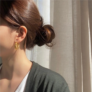 Detail of a gold twisted hoop earring worn by a model with soft natural lighting