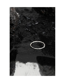 Detailansicht eines handgefertigten silbernen Hammerschlag-Rings auf nassem Lavagestein